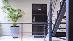 Una planta en maceta, una puerta oscura con placa de número y una escalera de metal.