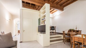 A living room with a sofa, TV, open shelving, dining table, chairs, and a staircase. - Apartment Giulietta in Florence by Mmega (Florence)
