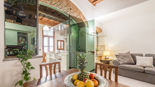 A dining area with a wooden table, a fruit bowl, and a green-framed glass door leading to a kitchen. - Apartment Giulietta in Florence by Mmega (Florence)
