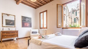 A bedroom with a bed, a dresser, a radiator, and a window with a view of buildings. - Apartment Giulietta in Florence by Mmega (Florence)