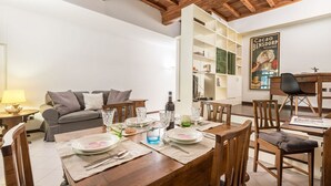 A dining area with a wooden table set for four, a sofa, and a bookshelf in the background. - Apartment Giulietta in Florence by Mmega (Florence)