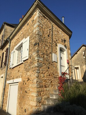 A stone building with white shutters, a chimney, and a small garden with red flowers. - Highly Rated, charming 14th century Toll House close to Solesmes and Sable (Avoise)