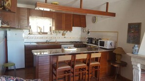A compact kitchen with wooden cabinets, a built-in microwave, and a small island with bar stools.
