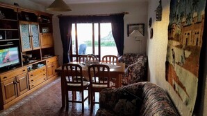 A living room with a dining table, chairs, a sofa, a television, and a large window with curtains.
