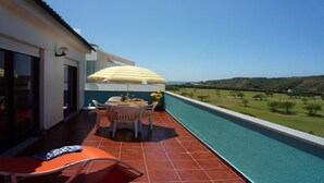 A balcony with a pool, a table with chairs, and an umbrella.