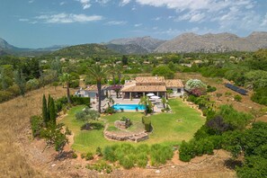 A villa with a swimming pool, surrounded by a landscaped garden and mountains in the background.