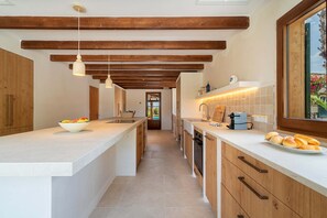 A modern kitchen with wooden beams, white countertops, and a view through a window.