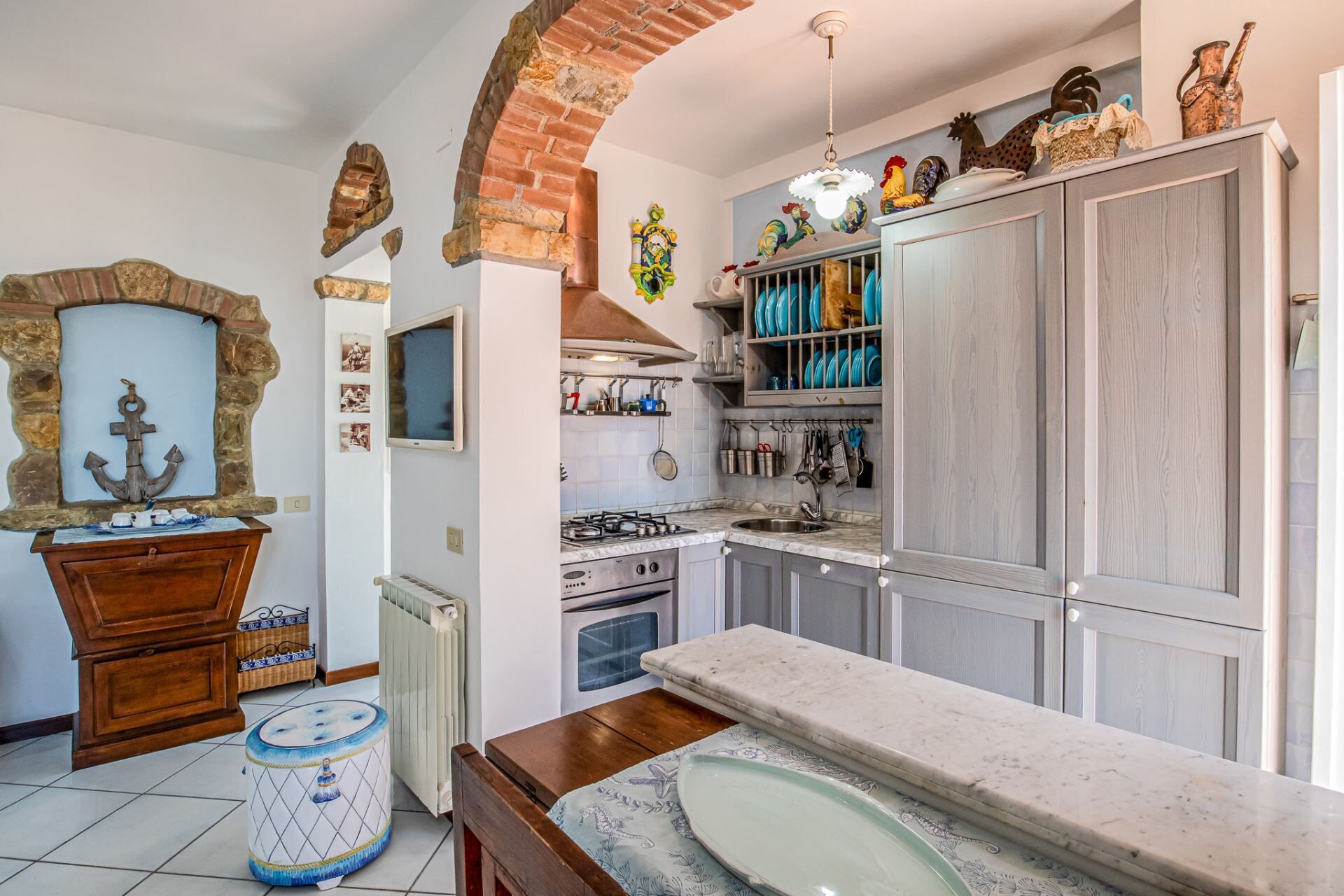 A kitchen with a brick archway, a stone fireplace, and a tiled floor.