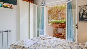 Une chambre à coucher avec un lit, un radiateur, une armoire et une vue sur un arbre par la fenêtre.