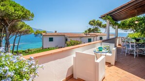 Une terrasse avec vue sur la mer, des bâtiments blancs et du mobilier d’extérieur.