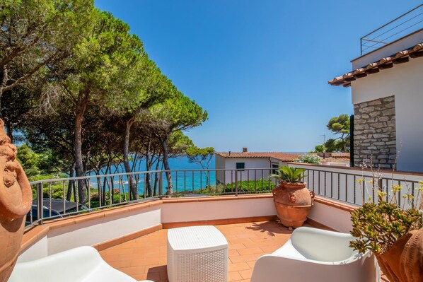 A balcony with a white table and chairs, potted plants, and a view of the sea. - Villa with private beach access (capoliveri Isola d'Elba)