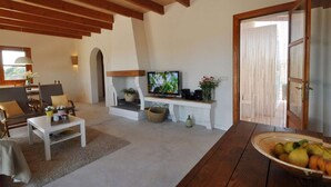 Uma sala de estar espaçosa com televisão, área de estar e uma mesa de madeira com frutas.