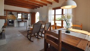 Ampla sala de estar com mesa de jantar de madeira, poltronas de balanço e uma grande janela.