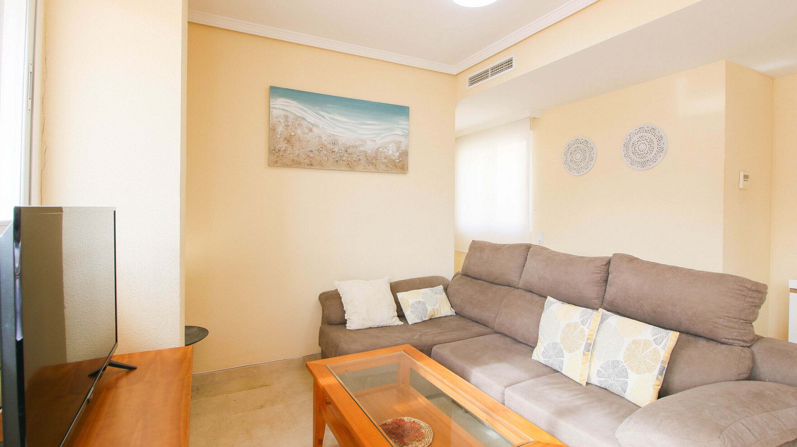 A living room with a sofa, a glass coffee table, and a painting on the wall.