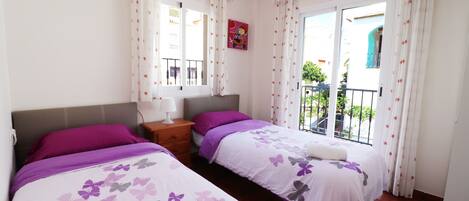 Une chambre avec deux lits, une table de chevet, une lampe et une fenêtre avec des rideaux.