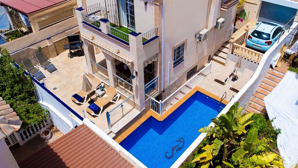 Um edifício de vários andares com piscina, área de estar ao ar livre e um carro estacionado nas proximidades.