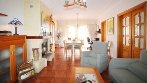 Uma sala de estar com sofá, poltrona, mesa de jantar e lareira.