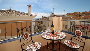 Varanda com mesa e cadeiras, uma garrafa de vinho e vista para prédios e o mar.