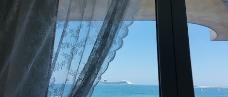 A view through a window with lace curtains, overlooking a body of water and a cruise ship.