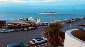 A coastal road with parked cars, a restaurant, and a cruise ship in the background.