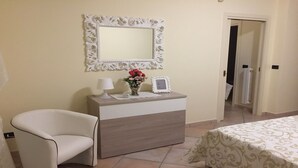 A hotel room with a bed, a chair, a dresser, a mirror, and a door leading to another room.