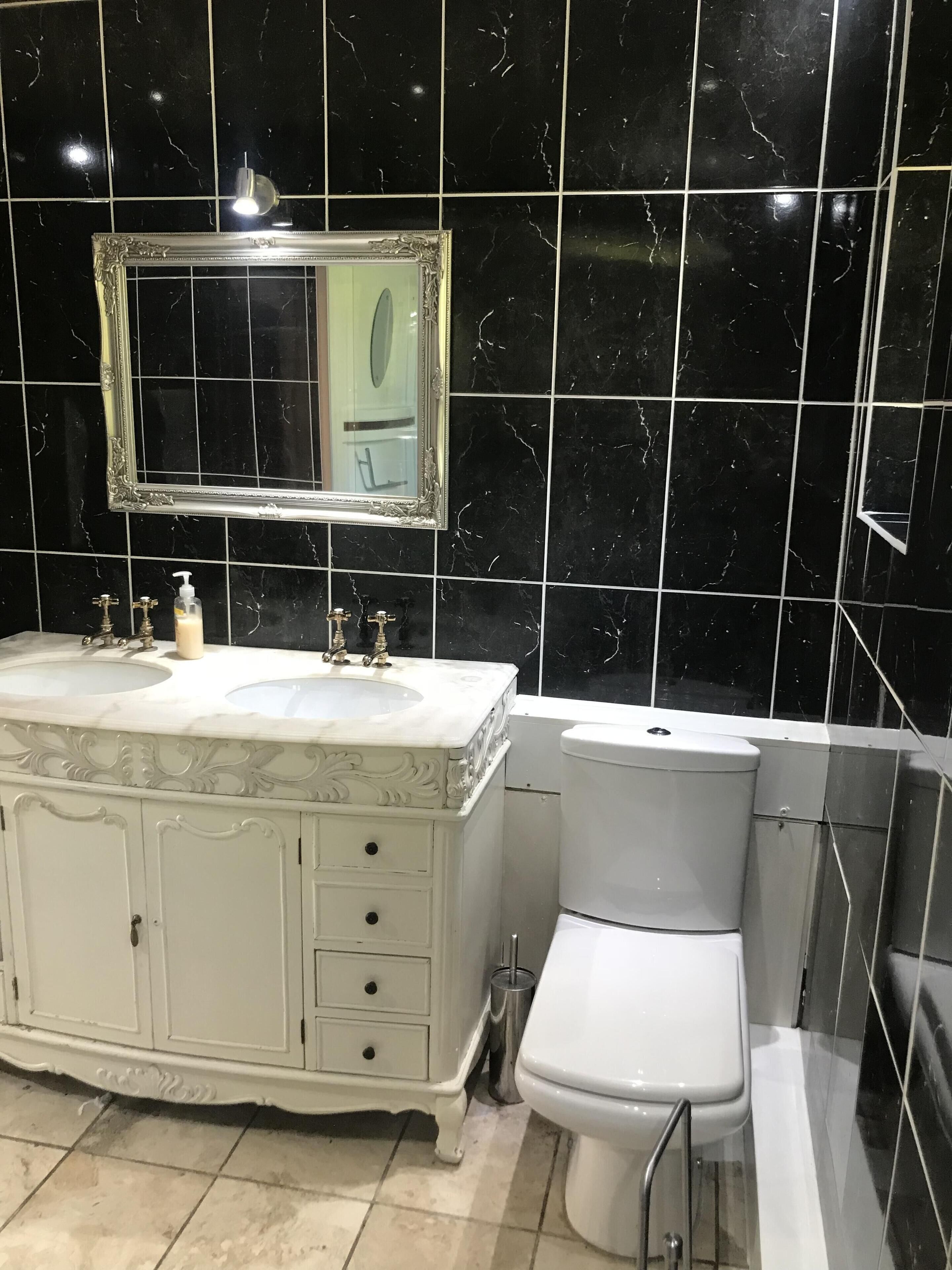A bathroom with a white vanity, a large mirror, a toilet, and black marble tiles.