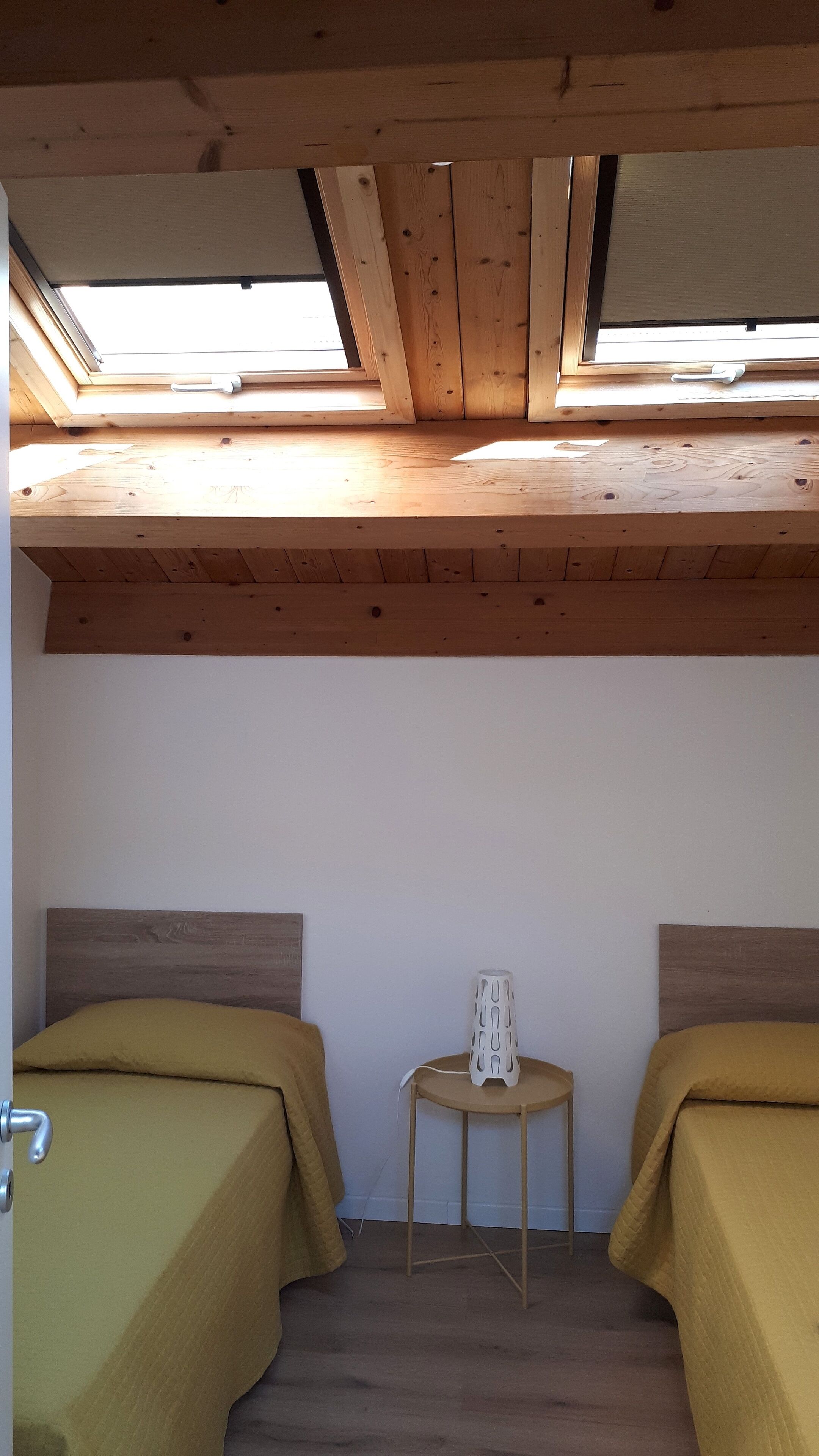 Una habitación con dos camas, una mesita con una lámpara y tragaluces.