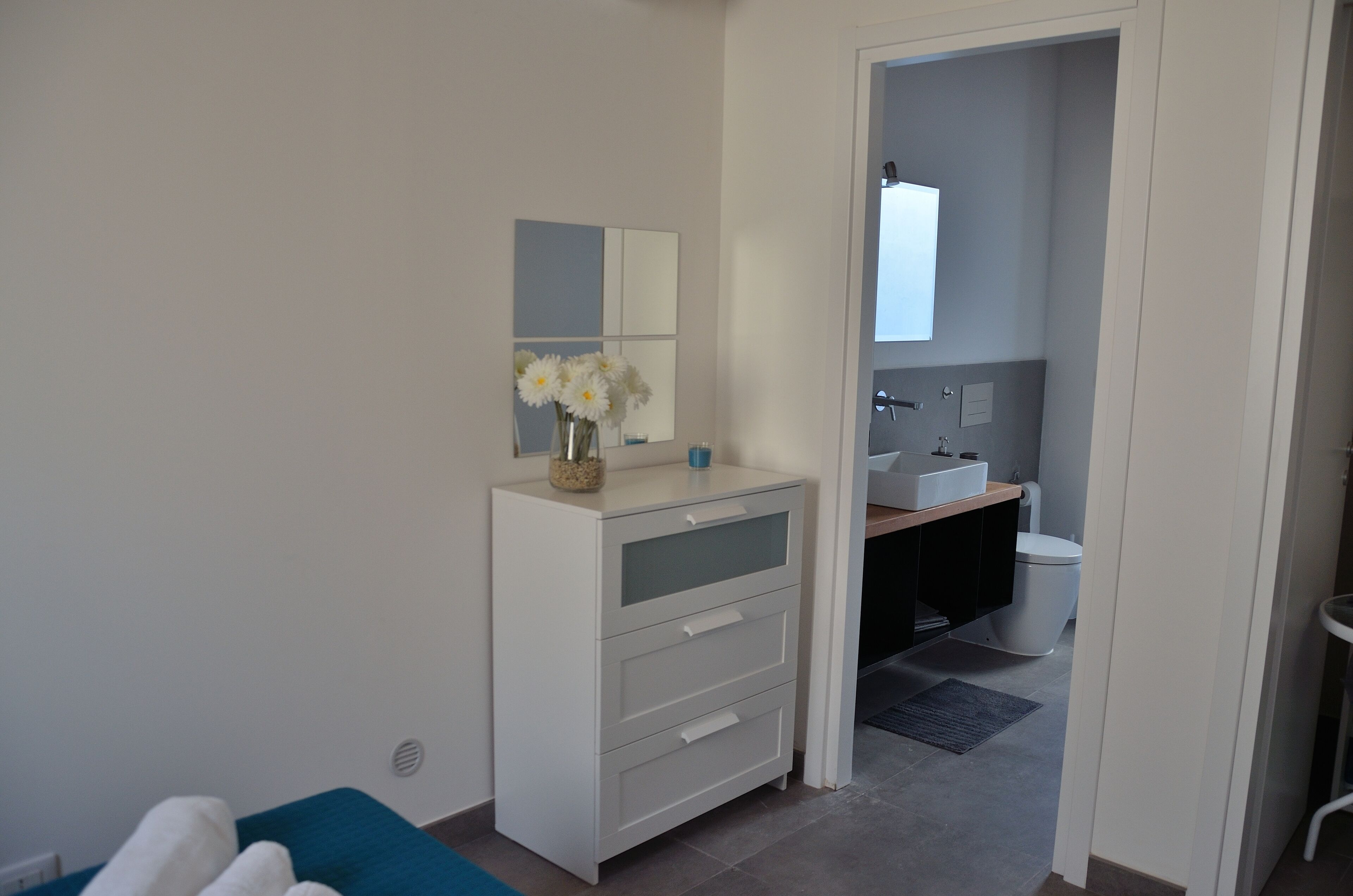 A modern bathroom with a white vanity, a mirror, and a vase with white flowers.
