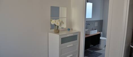 A modern bathroom with a white vanity, a mirror, and a vase with white flowers.