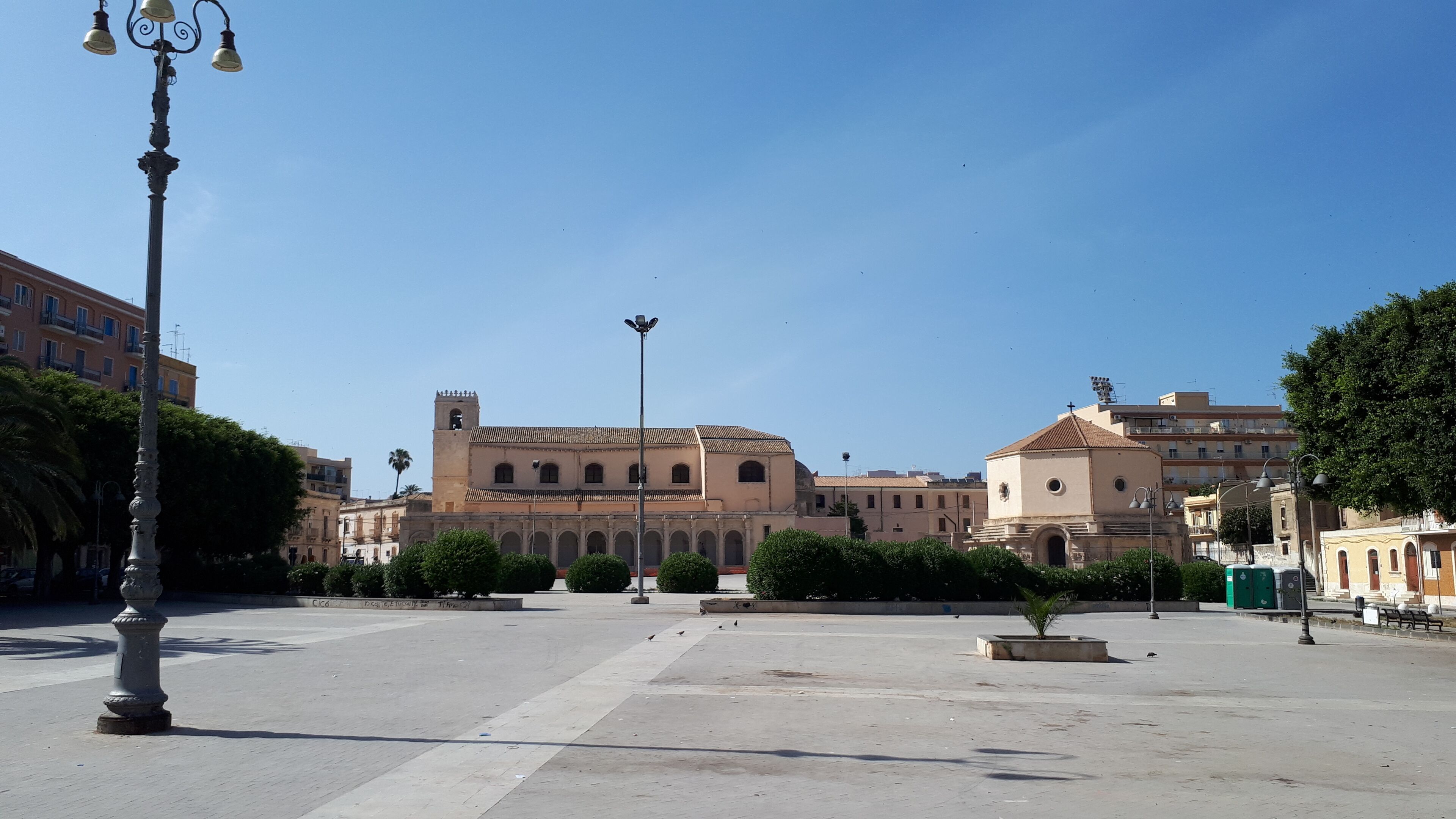 A spacious public square with a historic building featuring a bell tower and arched windows.