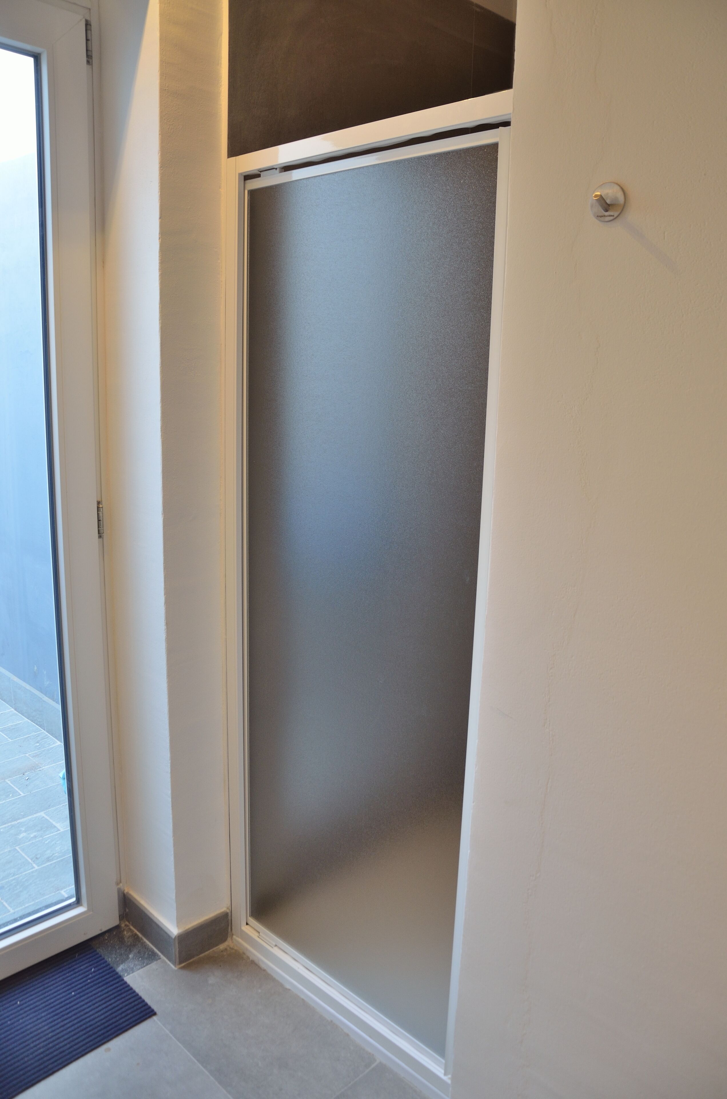 A room with a sliding door leading to a balcony, a door with a doorknob, and a textured wall.