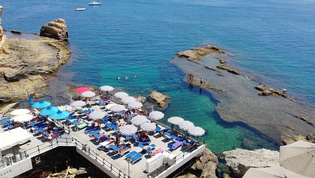 A coastal area with clear blue waters, rocky shores, and a boat with sun loungers and umbrellas. - New on Homeaway- totally renovated and air-conditioned independent house   (Siracusa)