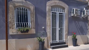 A building with a large arched window and a door with a metal gate, two air conditioning units mounted on the wall, and potted plants on the sidewalk. - New on Homeaway- totally renovated and air-conditioned independent house   (Siracusa)