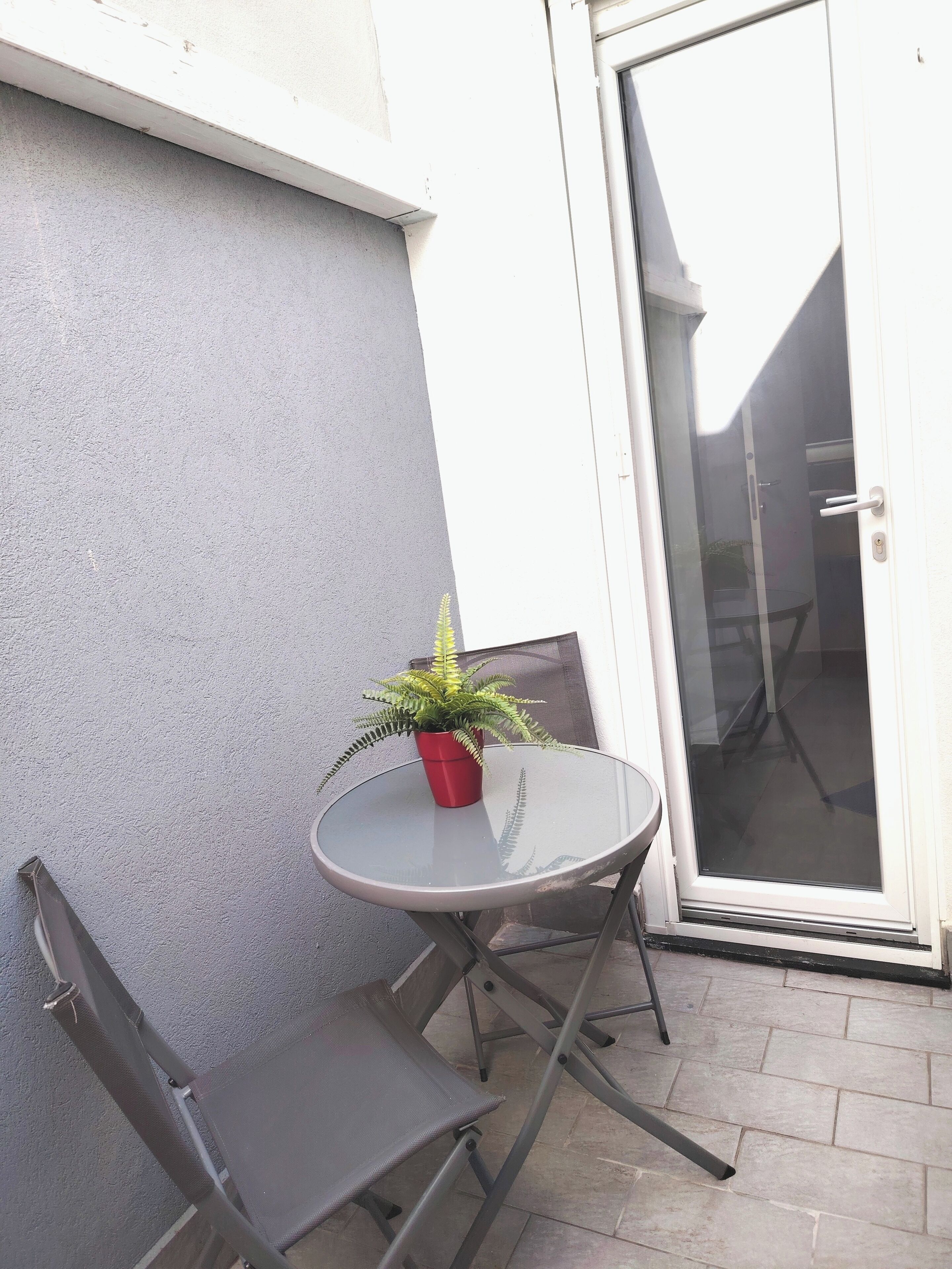 A small outdoor seating area with a table and chairs, a potted plant, and a sliding glass door.