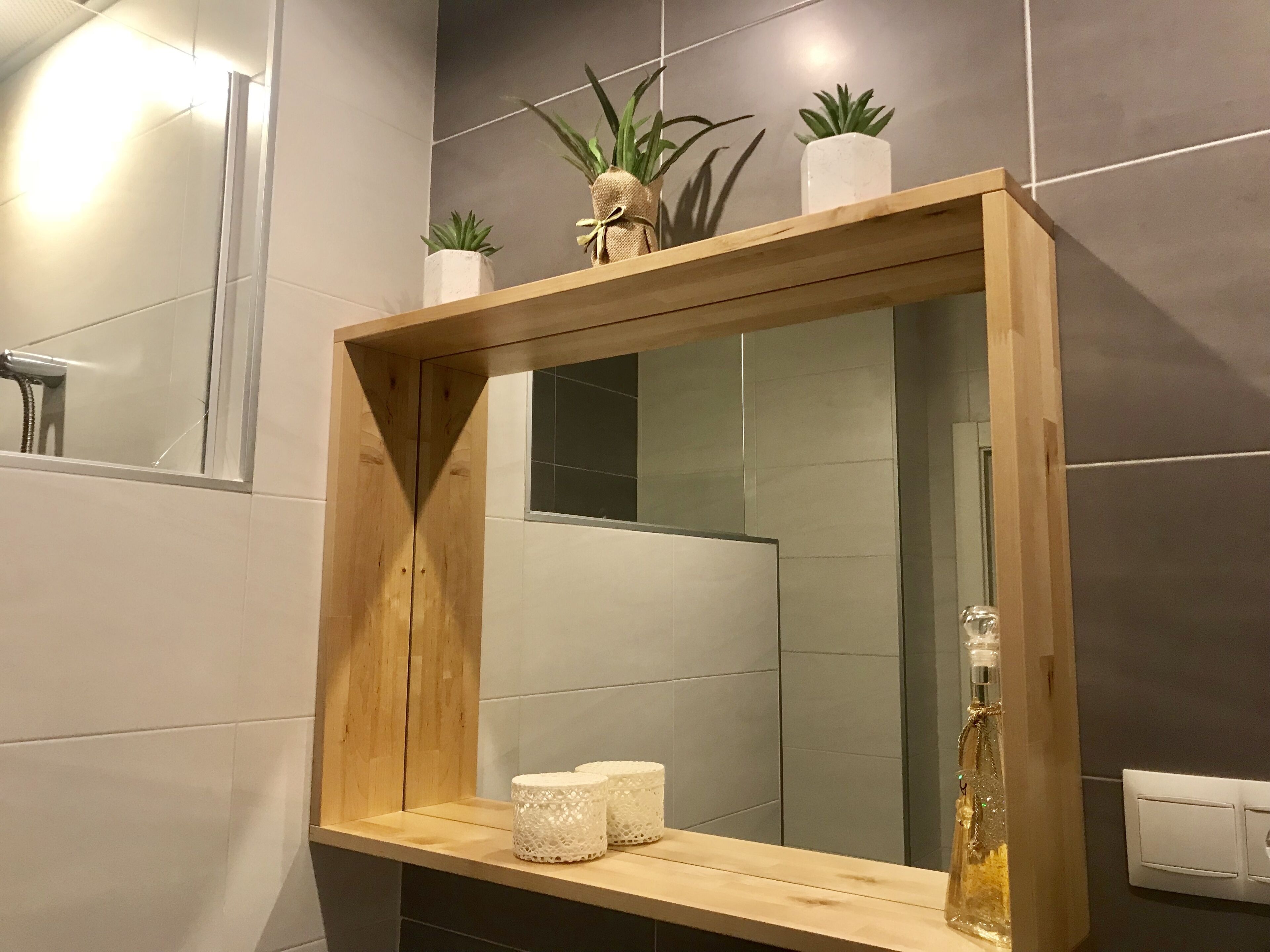 A bathroom with a wooden-framed mirror, a shelf with decorative items, and a tiled wall.