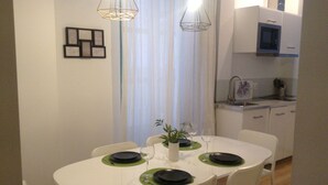 A dining area with a white table set for four, surrounded by white chairs. There is a kitchen area with a microwave and a sink visible in the background. -  Light and tranquility in the best location. Destiny Cathedral  (Málaga)