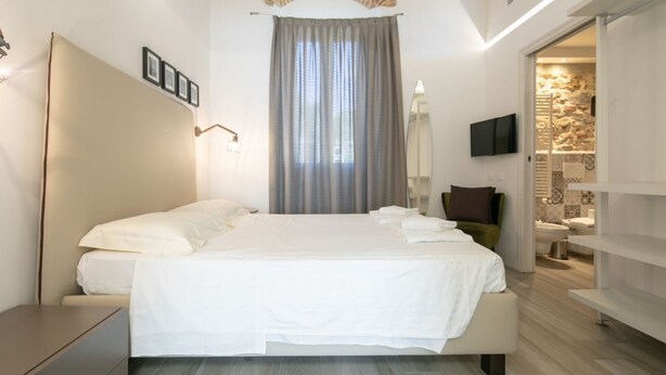 Une chambre d’hôtel moderne dotée d’un grand lit, d’une télévision à écran plat, d’une salle de bain avec un mur en pierre et offrant une vue sur la ville.