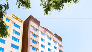 Un hotel de varios pisos con diseño moderno, que destaca un panel vertical de madera en la fachada, varios balcones y una variedad de locales comerciales en la planta baja.