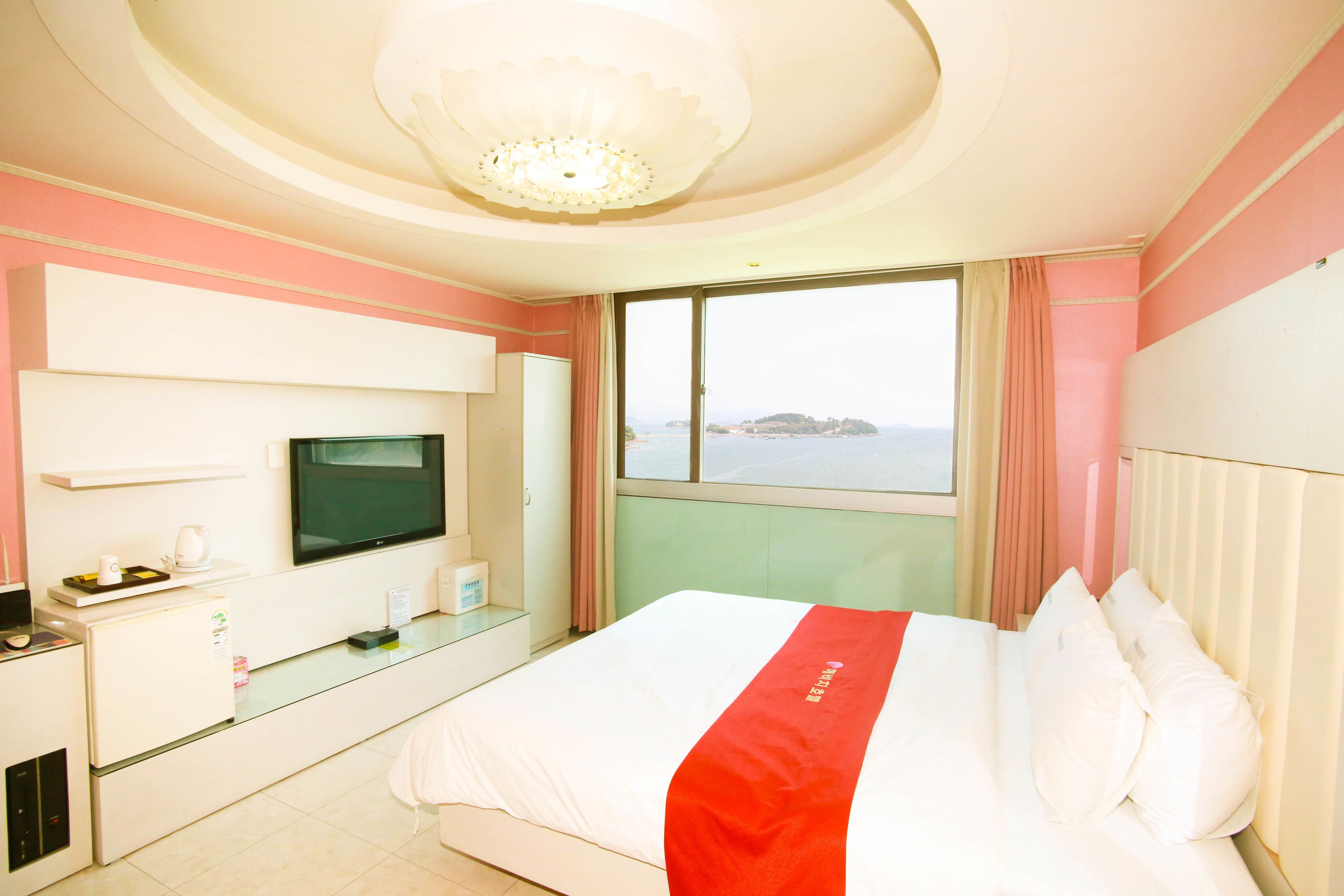 Una habitación de hotel con cama, televisor, escritorio con computadora y ventana con vista al mar.