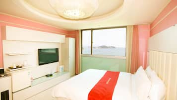Una habitación de hotel con cama, televisor, escritorio con computadora y ventana con vista al mar.