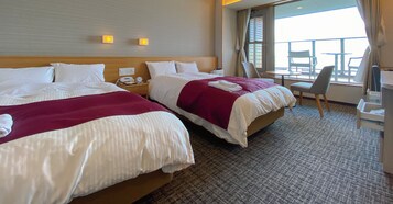 Quarto de hotel com duas camas, uma mesa e uma cadeira. Há uma janela com vista para o exterior.