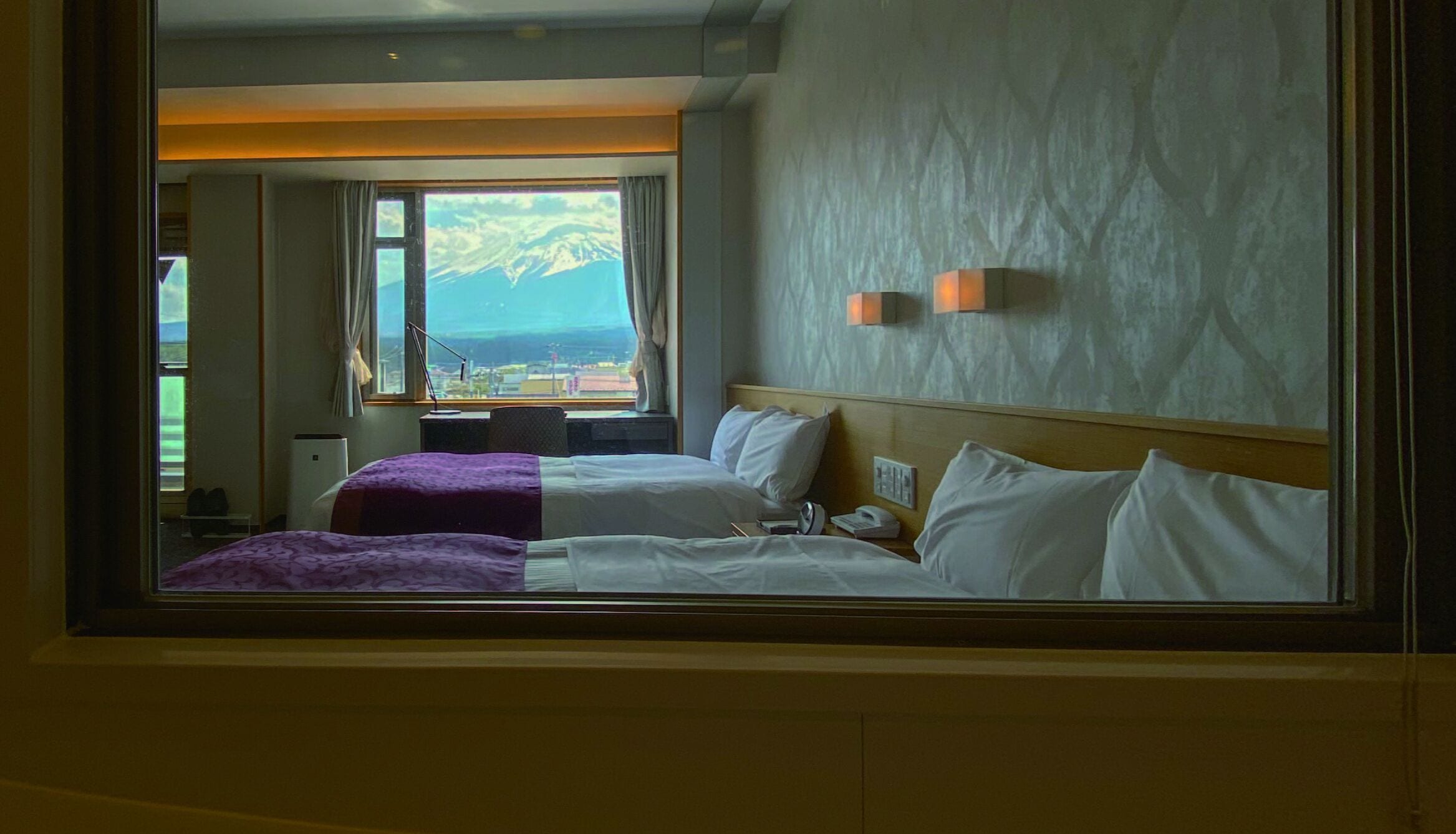 A hotel room with two beds, a view of mountains, and a window with curtains.