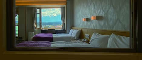 A hotel room with two beds, a view of mountains, and a window with curtains.