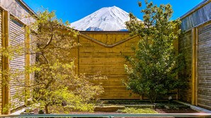 A pool area with a wooden fence, a view of a snow-capped mountain, and a small tree in the foreground. - The Noborisaka Hotel (Fujikawaguchiko)