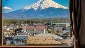 A view of Mount Fuji from a window overlooking a town with buildings and infrastructure. - The Noborisaka Hotel (Fujikawaguchiko)
