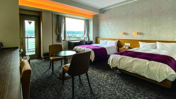 A hotel room with two beds, a desk, a chair, a small table, and a window with a view.