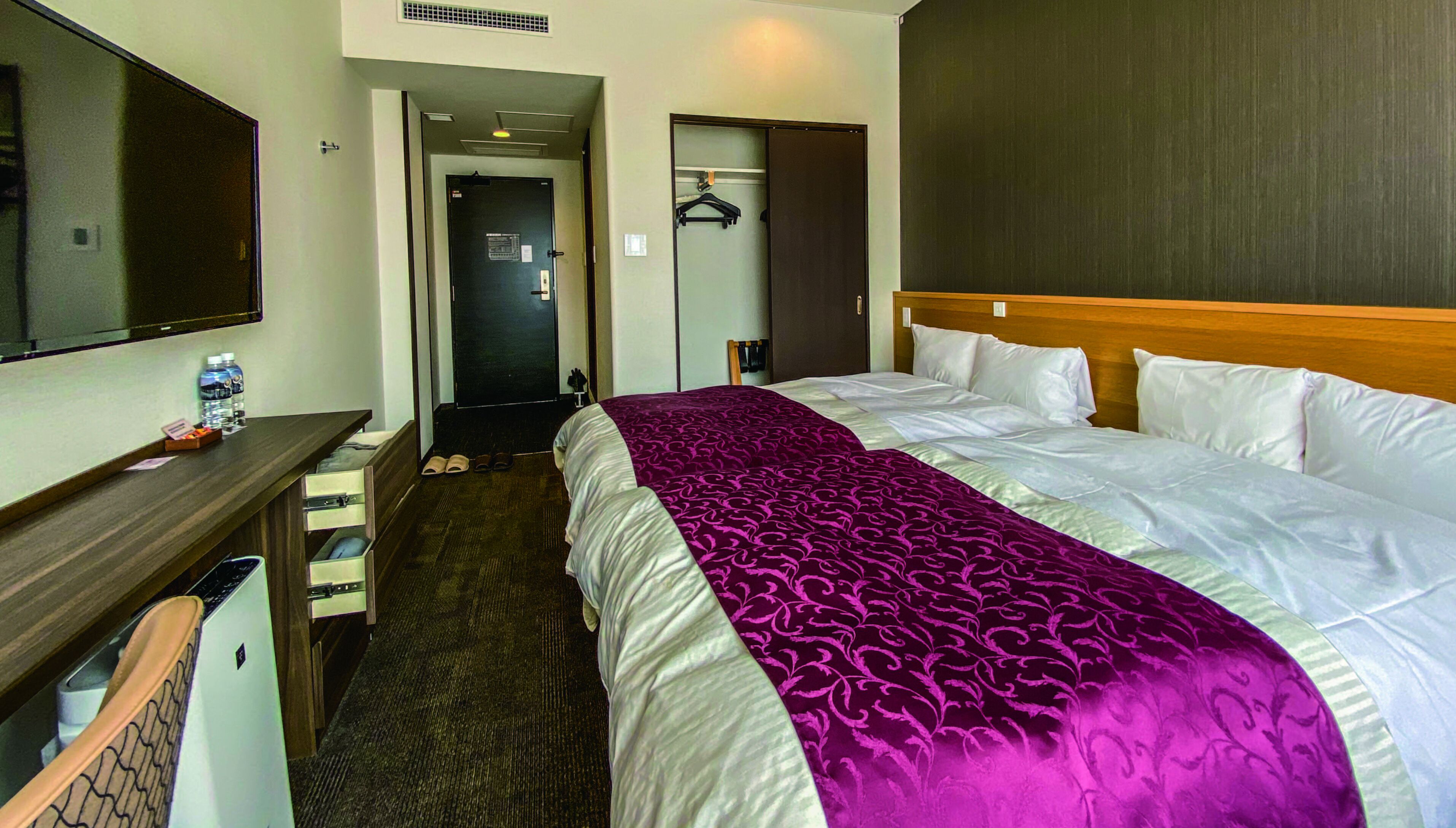 A hotel room with a large bed, a desk with a chair, a mirror, and a wardrobe.