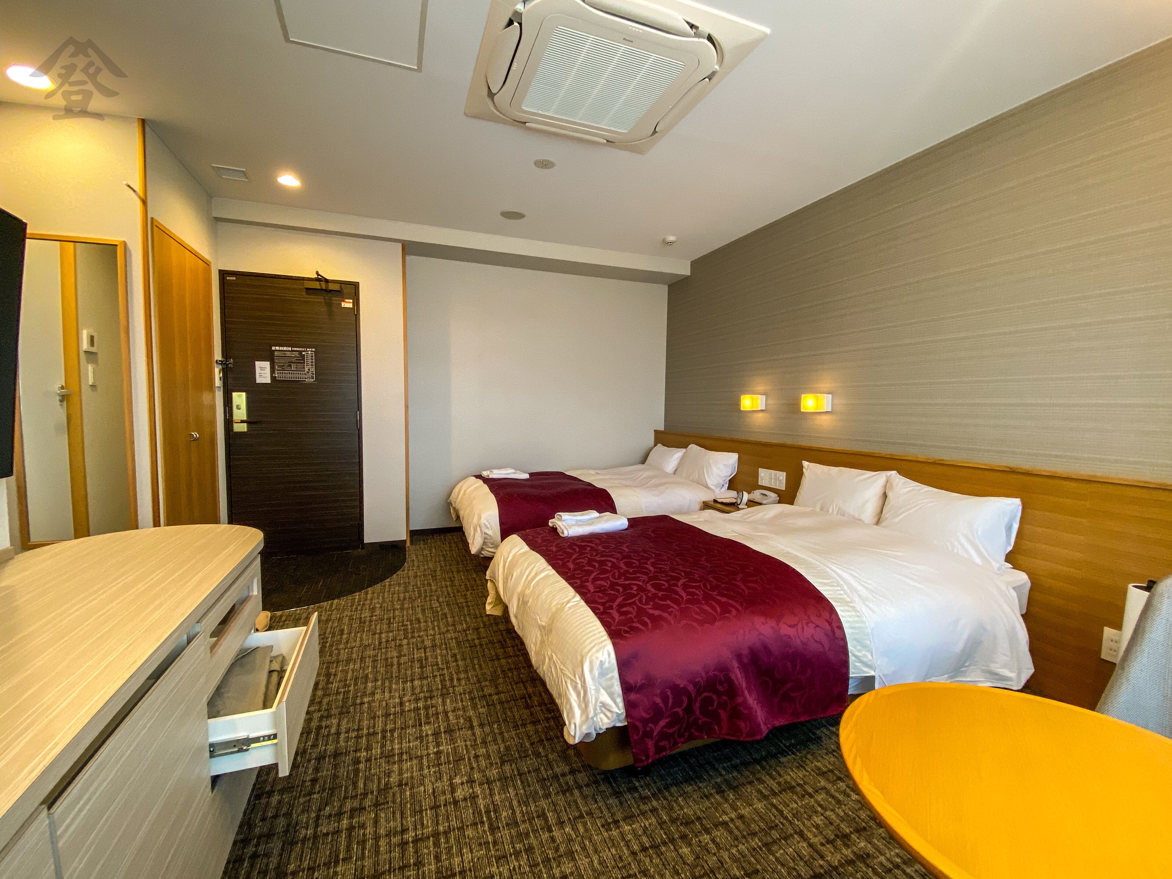 Habitación de hotel con dos camas, un escritorio, una silla y la puerta del baño.
