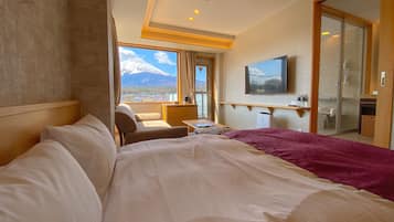 Habitación de hotel con una cama grande, escritorio, silla, televisor y vista a la montaña.