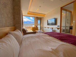 A hotel room with a large bed, a desk, a chair, a TV, and a view of a mountain.